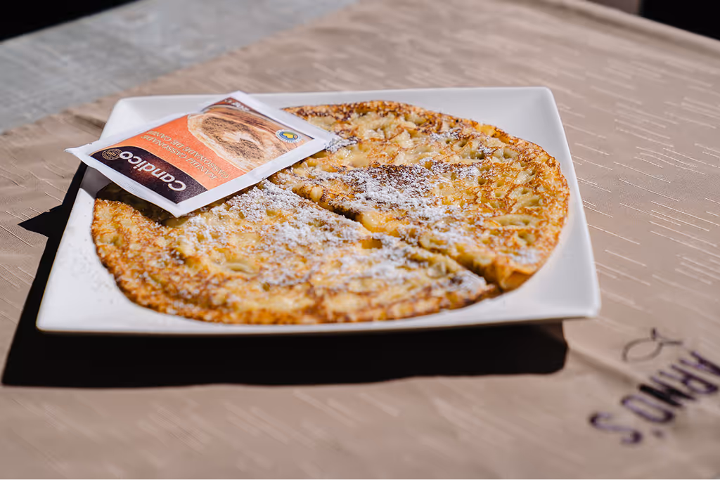 Plate with a sliced pancake dusted with powdered sugar and a small packet of cinnamon sugar on top.