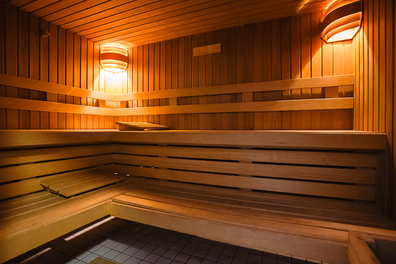 Interior of a wooden sauna with tiered benches and warm wall-mounted lights.
