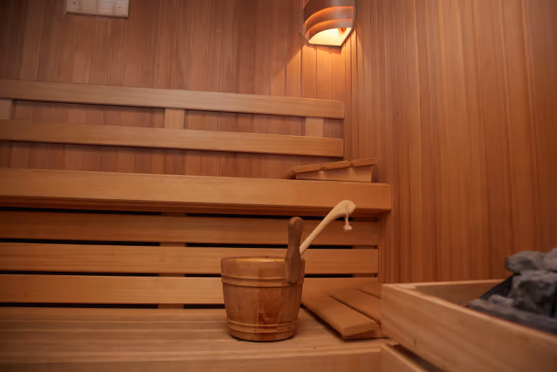 Interior of a wooden sauna with a bench, wooden bucket, ladle, and light fixture.